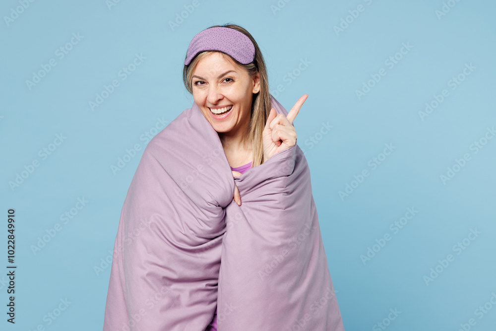 Calm young woman wear purple pyjamas jam sleep eye mask wrapped in duvet rest relax at home point index finger aside on area isolated on plain pastel light blue background Good mood night nap concept Calm young woman wear purple pyjamas jam sleep eye mask wrapped in duvet rest relax at home point index finger aside on area isolated on plain pastel light blue background Good mood night nap concept