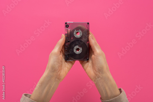 Female hands holding transparent audio cassette tape on pink background. Nostalgic hands holding an audio cassette, flat background, ideal for retro and archive imagery