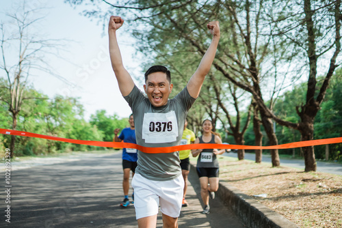 asian male runner crossing finish line celebrating victory with hands up gesture