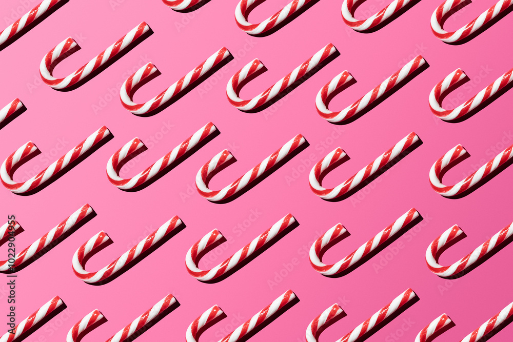 Top view of assorted red and white candy canes on pink background making a pattern