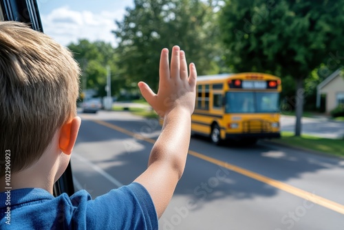 A young child waves goodbye to a school bus driving away, symbolizing back-to-school moments and childhood independence. photo