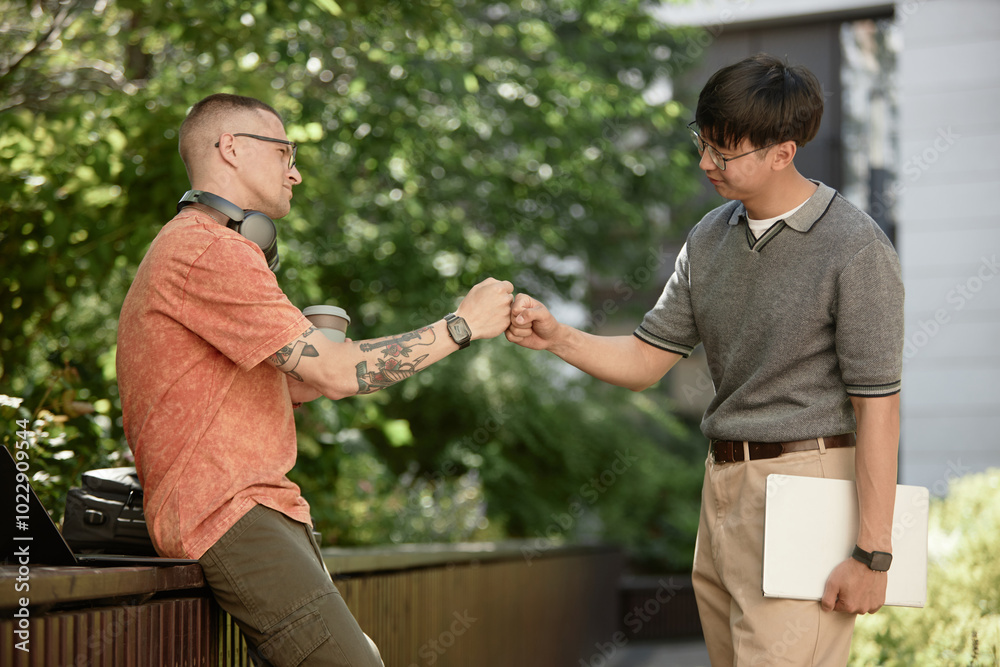 © Seventyfour - Side view of IT programmer bumping fists with partner making deal while having fun on meeting in park, copy space © Seventyfour - Side view of IT programmer bumping fists with partner making deal while having fun on meeting in park, copy space