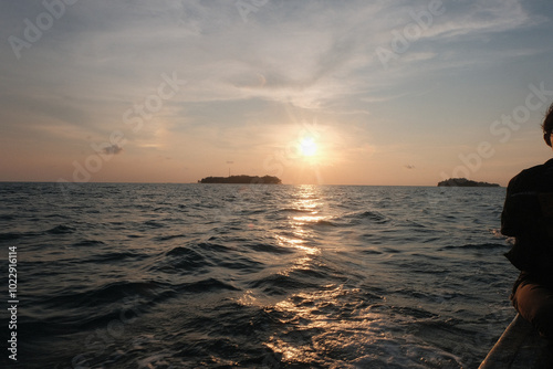 Stunning sunset over the ocean, where the sun dips below the horizon, casting vibrant oranges and purples across the sky. The tranquil waters reflect the colorful hues, creating a serene coastal scene
