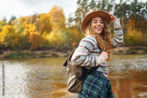 Female traveler with a backpack and a hat enjoying autumn hiking along the river. Active lifestyle. Hiking