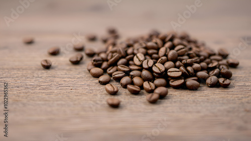 pile of roasted coffee beans on a wooden surface. The beans are scattered across the surface, with a few individual beans in the background.