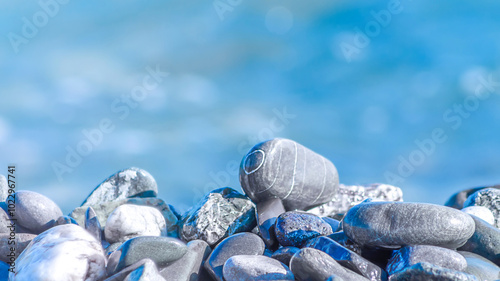 Sea pebble stones nature blue water background. Pebbles rock blue natural bokeh wallpaper, blur, soft focus.