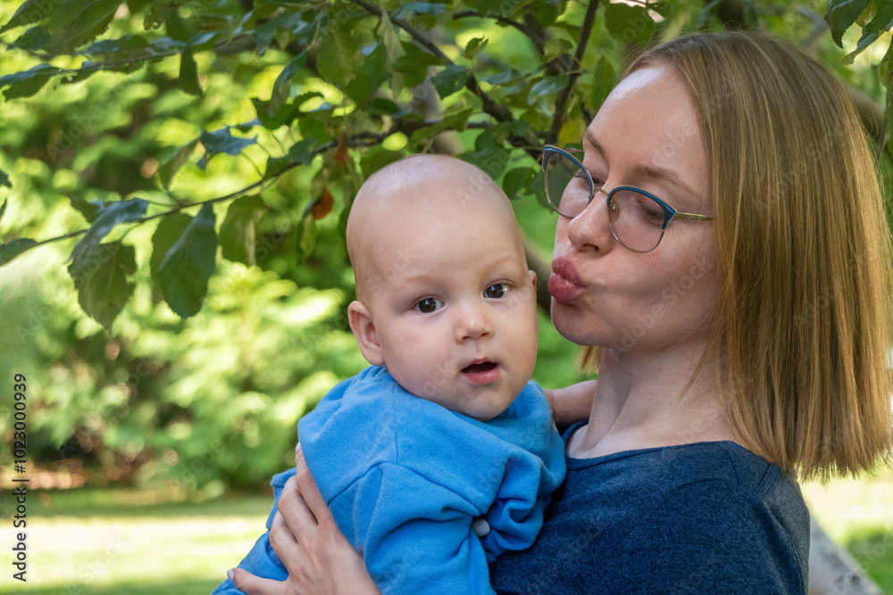Mama kissing baby. Happy mother holding her baby infant in her arms. Mother and son are playing in the garden. Mama and son matching blue outfits. Joy of parenting Mama kissing baby. Happy mother holding her baby infant in her arms. Mother and son are playing in the garden. Mama and son matching blue outfits. Joy of parenting