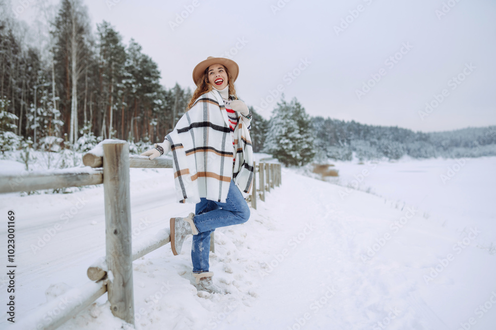 Fototapeta premium Portrait of a young smiling woman in hat, scarf, and sweater in winter time outdoors. Fashion. Enjoying nature. Boho style.
