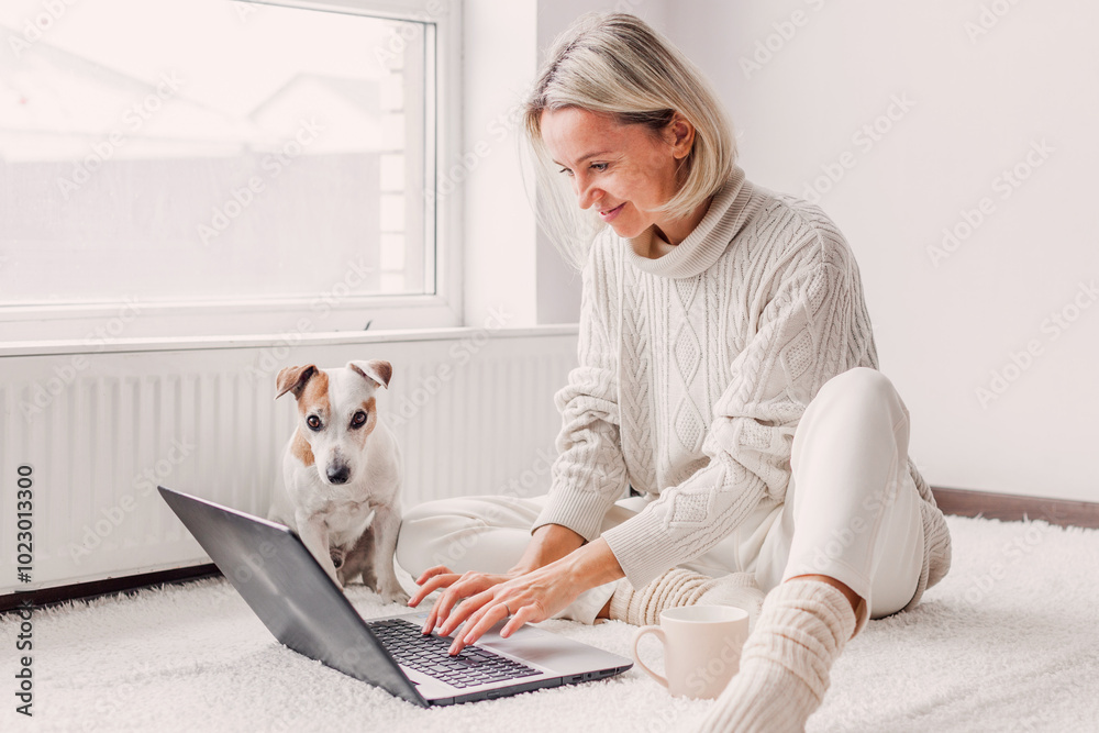 © Tatyana Gladskih - Happy middle aged woman with dog using her laptop at cozy white home © Tatyana Gladskih - Happy middle aged woman with dog using her laptop at cozy white home