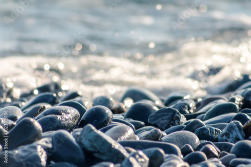 Sea shore landscape nature wallpaper. Pebble gravel stones, sea water on beach close up, defocused natural bokeh lights background. Dark grey wet pebble gravel stones, blur, soft focus.