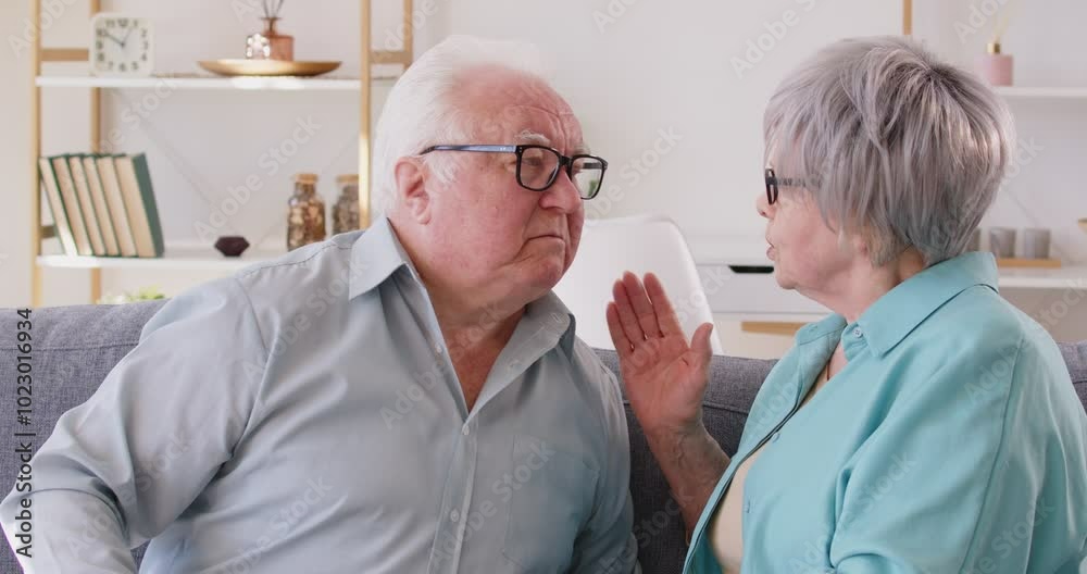 Age-related hearing problems in elderly. Elderly man leans over to woman and puts his hand to ear, demonstrating that he is hard of hearing. Woman is trying to talk to man who can't hear her well.