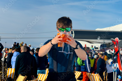 Young male skier holding drinks at an Apres Ski event. Apres ski event at Les Menuires ski resort in the three valleys, France