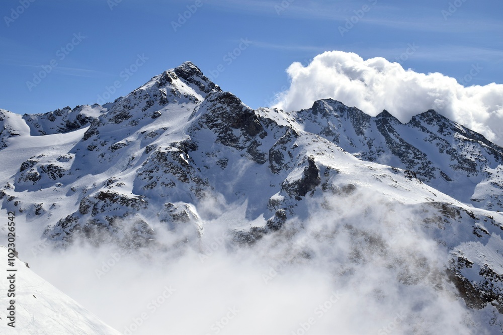 Obraz premium Snowcapped Alpine mountains peaking through clouds in the Three Valleys, France. Breathtaking view from ski resort in French Tarentaise Valley.