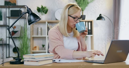 Woman in glasses working at home desk with documents and laptop information simultaneously drinking cup of tea photo