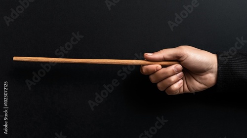 Hand holding a long wooden stick against a dark background, demonstrating a grasping gesture.