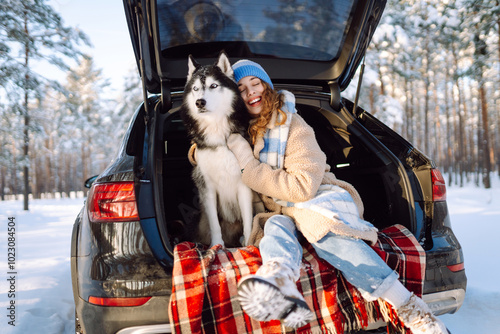 Young woman in winter clothes sitting in the trunk of a car with her husky and play. Winter holidays. Travel concept