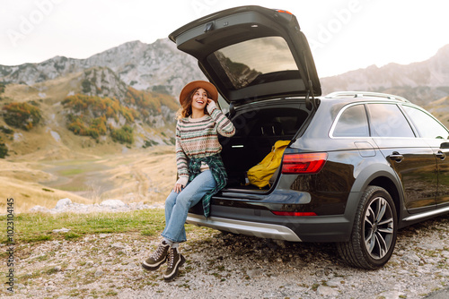 Young woman enjoying autumn nature while sitting in the trunk of her car during a solo trip. Road trip. Travel. tourism concept. Autumn Morning.