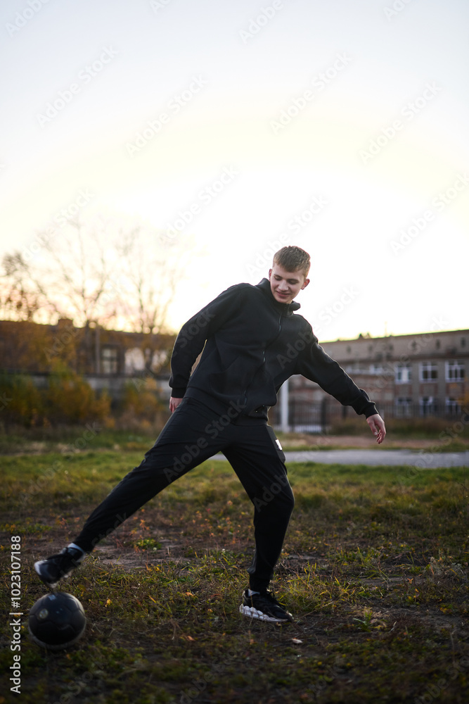 Young guy in black sportswear playing football on sports ground Young guy in black sportswear playing football on sports ground