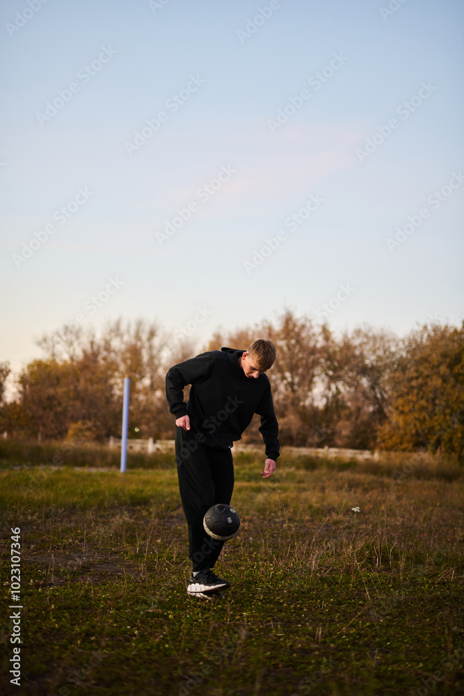 Young guy in black sportswear playing football on sports ground Young guy in black sportswear playing football on sports ground