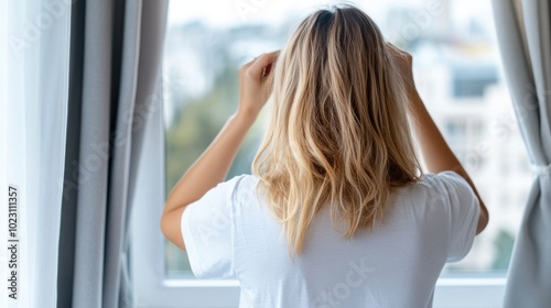 A woman is seen gazing out a window, seemingly lost in thought while observing the world outside, reflecting contemplation and introspection in a modern setting.