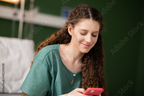 Young woman in recovery after surgery, scrolling through her phone, staying connected with friends and family online.