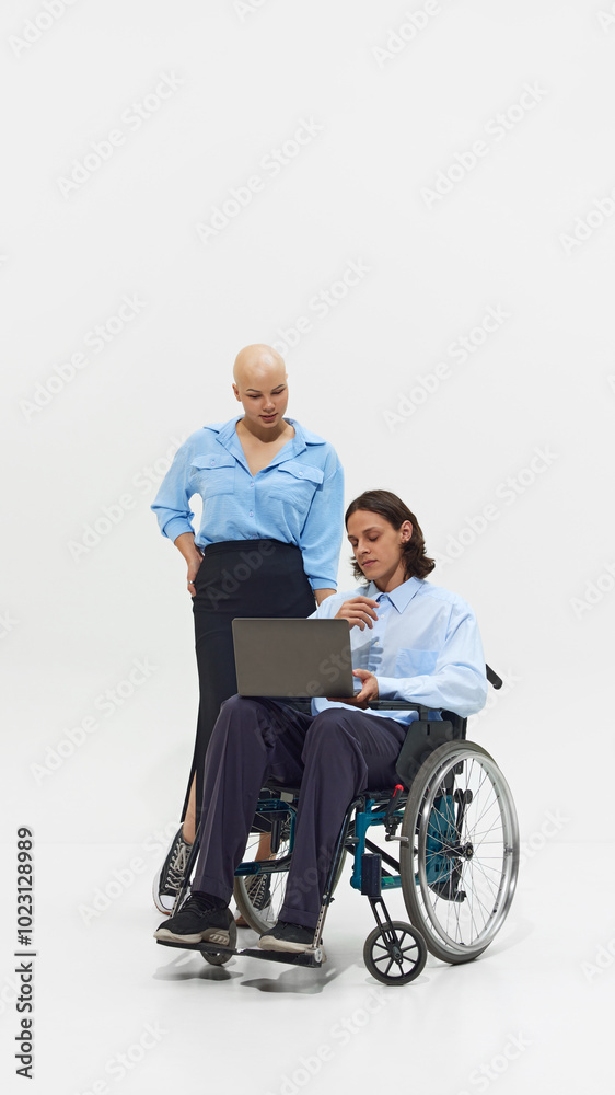 Young bald woman in blue shirt standing next to man in wheelchair working on laptop, showcasing inclusivity and collaboration in workplace. Concept of business, dei, equality, support Young bald woman in blue shirt standing next to man in wheelchair working on laptop, showcasing inclusivity and collaboration in workplace. Concept of business, dei, equality, support