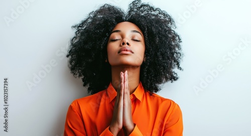 A young woman with curly black hair praying with her eyes closed