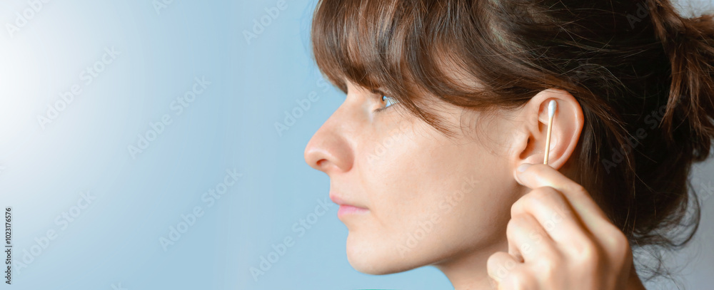 young woman is seen from the side, gently cleaning her ear with a cotton swab. Her long hair cascades over her shoulder, and she has a focused expression as she takes care of her personal hygiene. Th young woman is seen from the side, gently cleaning her ear with a cotton swab. Her long hair cascades over her shoulder, and she has a focused expression as she takes care of her personal hygiene. Th