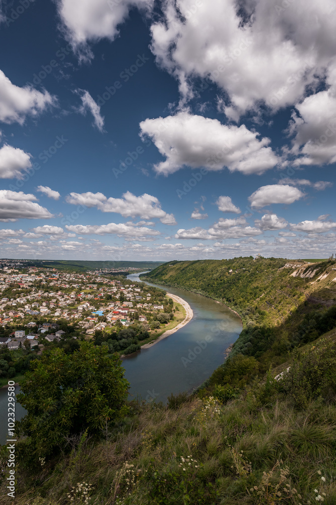 Serene Aerial View of a Winding River Surrounded by Lush Green Hills and a Quaint Town Under a Cloudy Sky Serene Aerial View of a Winding River Surrounded by Lush Green Hills and a Quaint Town Under a Cloudy Sky