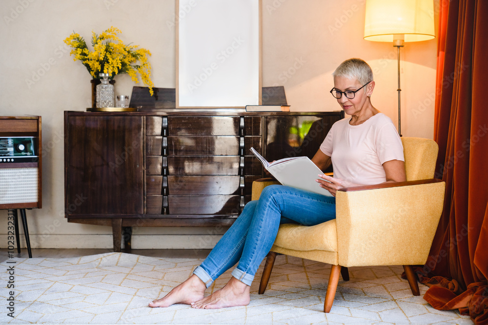 Senior mature elderly caucasian woman housewife relaxing in armchair while reading fashion magazine in living room at home, looking for news information Senior mature elderly caucasian woman housewife relaxing in armchair while reading fashion magazine in living room at home, looking for news information
