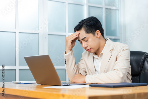 Professional Asian businessman working in his office reviewing work, planning strategy, creative thinking and innovation ideas, feeling sad upset having headache sitting at desk on laptop computer.