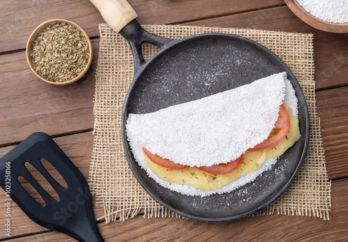 Traditional brazilian cheese and tomato stuffed tapioca on a pan with ingredients photo