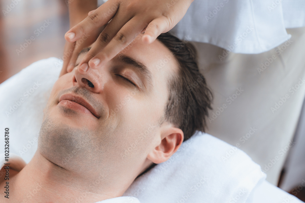 Caucasian man enjoying relaxing anti-stress head massage and pampering facial beauty skin recreation leisure in dayspa modern light ambient at luxury resort or hotel spa salon. Quiescent Caucasian man enjoying relaxing anti-stress head massage and pampering facial beauty skin recreation leisure in dayspa modern light ambient at luxury resort or hotel spa salon. Quiescent