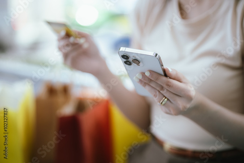 A stylish Asian woman is happily shopping in the city, holding several bags and a credit card. She lives in a lively city and enjoys holiday deals and promotions as a smart shopper.