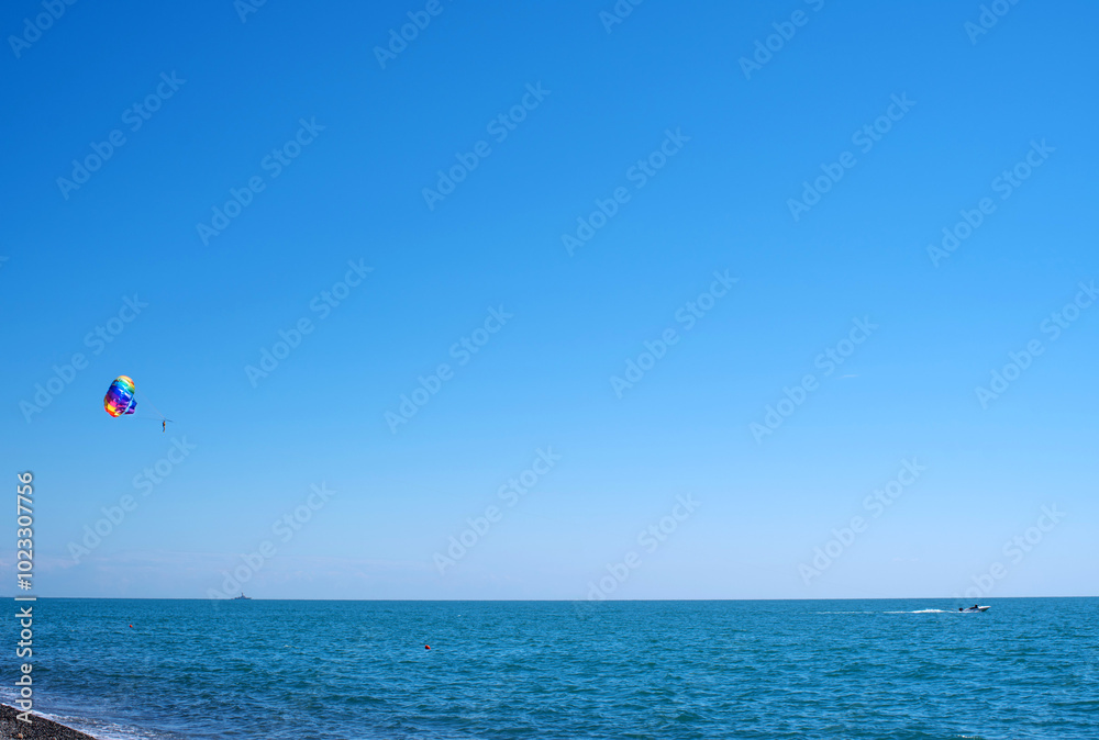 Tourists fly on a bright paraglider against the blue sky in the summer on a sunny day. Beach holidays, tourist marine entertainment. Parasailing Tourists fly on a bright paraglider against the blue sky in the summer on a sunny day. Beach holidays, tourist marine entertainment. Parasailing