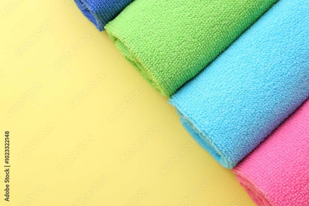 Rolled different microfiber cloths on yellow background, top view. Space for text Rolled different microfiber cloths on yellow background, top view. Space for text
