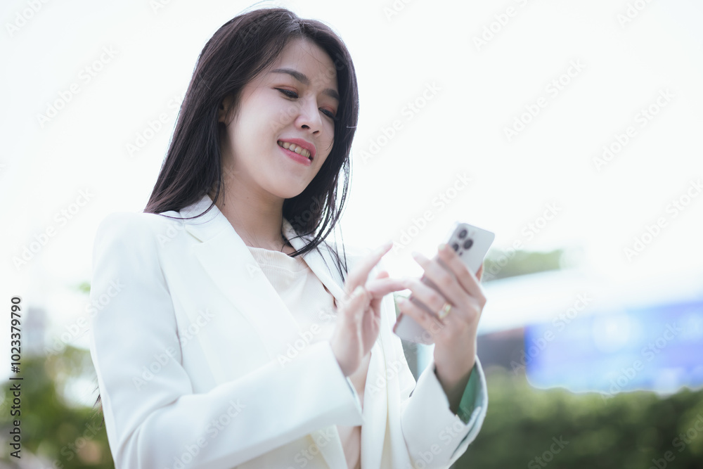 Confident Asian businesswoman in urban suit smiles as she types on her smartphone, balancing a career in digital finance, online e-commerce, and global business opportunities. Confident Asian businesswoman in urban suit smiles as she types on her smartphone, balancing a career in digital finance, online e-commerce, and global business opportunities.