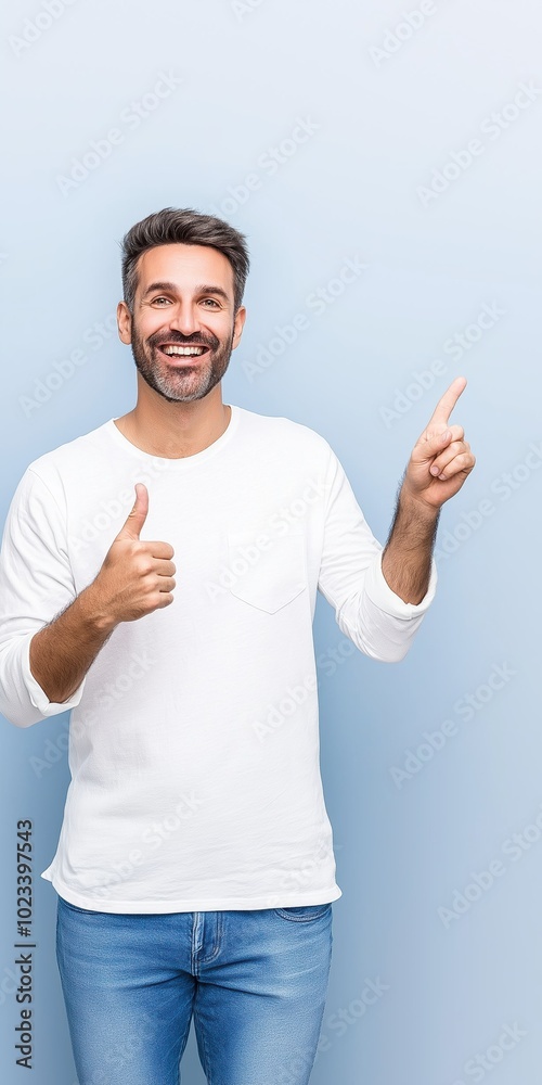 A man in a white shirt and blue jeans is pointing to the sky. He is smiling and he is giving a thumbs up