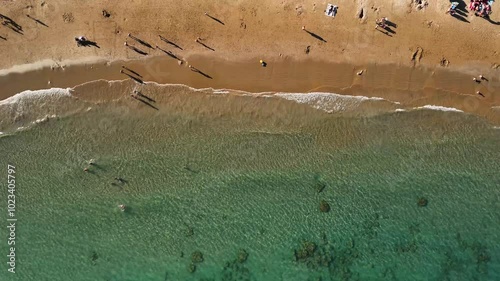 Crystal clear water beach with people bathing and playing on the seashore. Silhouettes of the shadows of people. Top view from drone. Wallpaper with movement