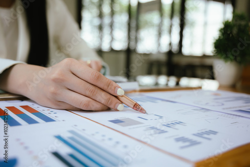 A businesswoman sits at her desk, calculating financial data on her laptop. Surrounded by paperwork and charts, she analyzes expenses and income, reflecting her role in corporate finance and accountin photo