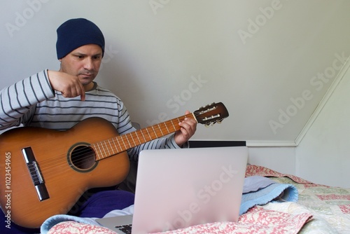 latino man lying in bed with guitar and laptop computer photo