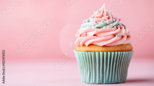 Delicious cupcake with pastel pink and blue frosting, topped with sprinkles, set against a soft pink background, perfect for dessert and celebration themes.