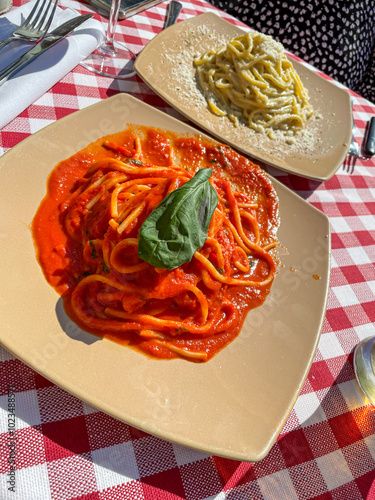 Two plates on an outdoor table in Rome: creamy tagliatelle carbonara and vibrant spaghetti al pomodoro, capturing the essence of Italian cuisine under the warm Mediterranean sun.