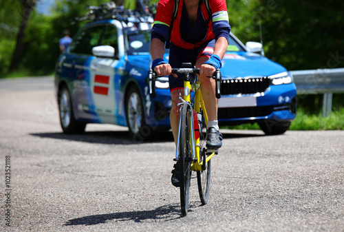 cyclist with racing bike pedaling uphill during training and the sports team car following him to assistance