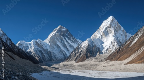 Panoramic view of snow-capped mountains against a clear blue sky with a valley in the foreground.