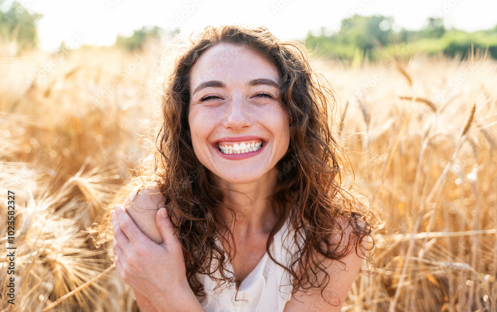 Happy beautiful woman smiling at camera in a wheat field - Delightful female enjoying summertime sunny day outside - Wellbeing, mental health, body care and happiness concept Happy beautiful woman smiling at camera in a wheat field - Delightful female enjoying summertime sunny day outside - Wellbeing, mental health, body care and happiness concept