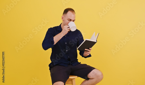 Young man enjoying peaceful reading session with coffee. Yellow background