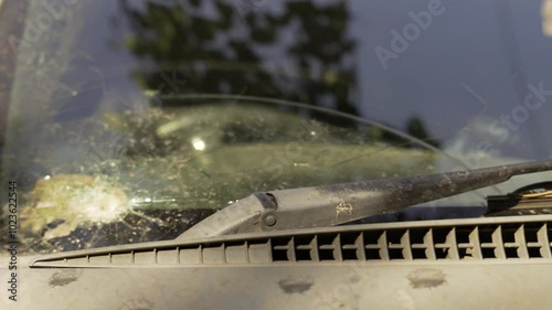 A bullet hole shatters the window of an abandoned vehicle, evidence of combat action. The rusted frame and broken glass depict the aftermath of a military mission or battlefield encounter.