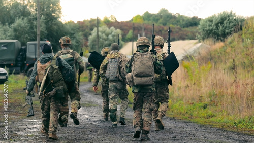 Soldiers marching in formation with military gear. A group of soldiers are seen walking away along a muddy path, dressed in full military camouflage and carrying rifles. photo