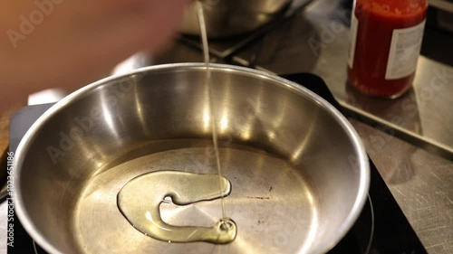 Pouring oil, shiny surface, food prep. Close-up oil being poured into hot stainless steel pan on stovetop, initial steps of food preparation, highlighting common cooking process in kitchen setting. photo